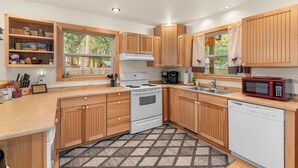 A modern kitchen with wooden cabinets, a white stove, a microwave, and a dishwasher. - Cozy cabin, dogs ok, hot tub, & fireplace (Leavenworth)
