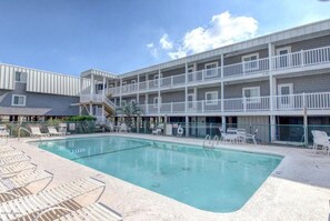 A pool area with lounge chairs and a multi-story building with balconies. - 3 br, 2 ba condo walking distance to beach (Ocean Isle Beach)