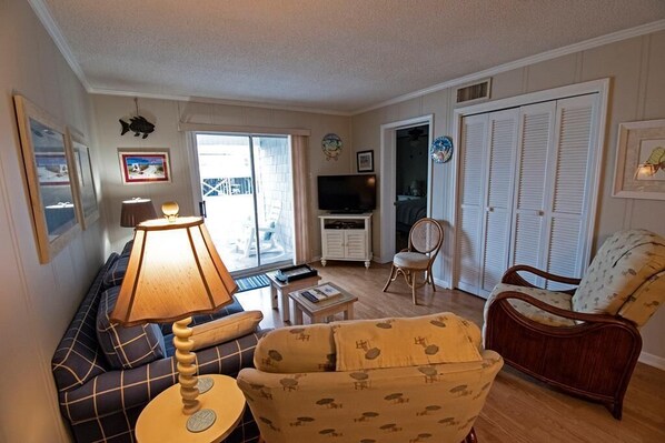 A living room with a sofa, armchair, TV, and a lamp. - 3 br, 2 ba condo walking distance to beach (Ocean Isle Beach)