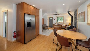 A modern kitchen with wooden cabinets, a stainless steel refrigerator, and a dining area with a round table and chairs. - A cozy dog friendly cabin, sleeps 6 with a hot tub (Leavenworth)