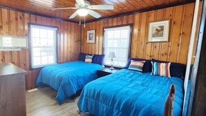 Een kamer in chaletstijl met twee bedden, houten wanden, een plafondventilator en een raam met jaloezieën.