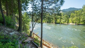 Un pontile in legno che si affaccia su un fiume, circondato da una fitta foresta e montagne sullo sfondo.