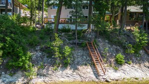 Una proprietà lungo il fiume con una scala in legno che conduce a un edificio, immersa tra alberi e una sponda rocciosa.
