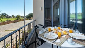 Ein Balkon mit einem für das Frühstück gedeckten Tisch, mit Blick auf eine Rasenfläche.