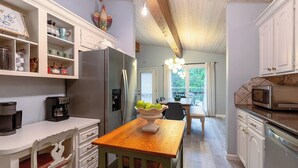 Una cocina con muebles blancos, una mesa de madera y vistas al comedor.