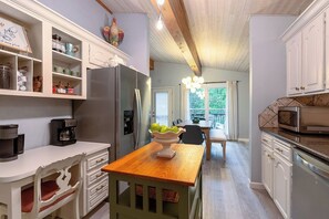 Una cocina con muebles blancos, una mesa de madera y vistas al comedor.