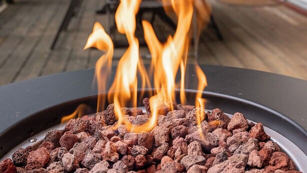 Un patio con una parrilla de carbón, mobiliario exterior e iluminación con luces colgantes.