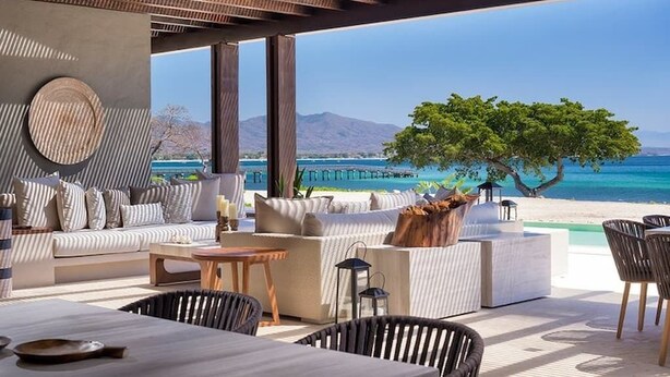 Eine moderne Lounge-Bereich im Freien mit einer Sofagruppe, einem Esstisch und Stühlen mit Blick auf Strand und Meer.