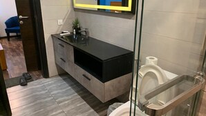 A modern bathroom with a glass shower enclosure, a toilet with a bidet attachment, a black vanity with a mirror, and a small potted plant. - Charming 1-bedroom apartment with AC in vibrant Islamabad (Islamabad)