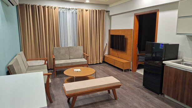 A hotel room with a sofa, a small round table, a bench, a TV, a refrigerator, and a kitchenette. - Charming 1-bedroom apartment with AC in vibrant Islamabad (Islamabad)