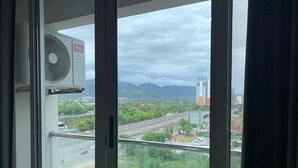 A window with a view of a cityscape, including a highway, buildings, and mountains. - Charming 1-bedroom apartment with AC in vibrant Islamabad (Islamabad)