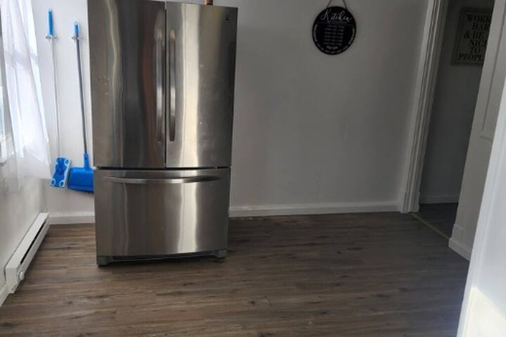 A stainless steel refrigerator in a room with wooden flooring and white walls.