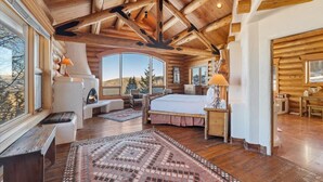Un dormitorio de cabaña de troncos con una cama grande, vigas de madera en el techo y vistas a las montañas.