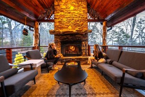 Ein gemütliches Cabin-Interieur mit Kamin aus Stein, Holzmöbeln und Blick auf den Wald.