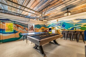 Ein Billardtisch mit Holzrahmen und Spielstock, ein Barbereich mit Barhocker und ein Wandgemälde an der Wand.