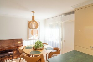 Un coin repas comprenant une table ronde, des chaises, un banc, un luminaire suspendu, une plante en pot et une fenêtre avec des rideaux.