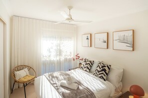 Une chambre à coucher comprenant un lit, une chaise, un ventilateur de plafond et trois tableaux encadrés accrochés au mur.