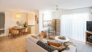 Un soggiorno con divano, tavolino e poltrone. Si notano anche un tavolo da pranzo con sedie e una ventola a soffitto.
