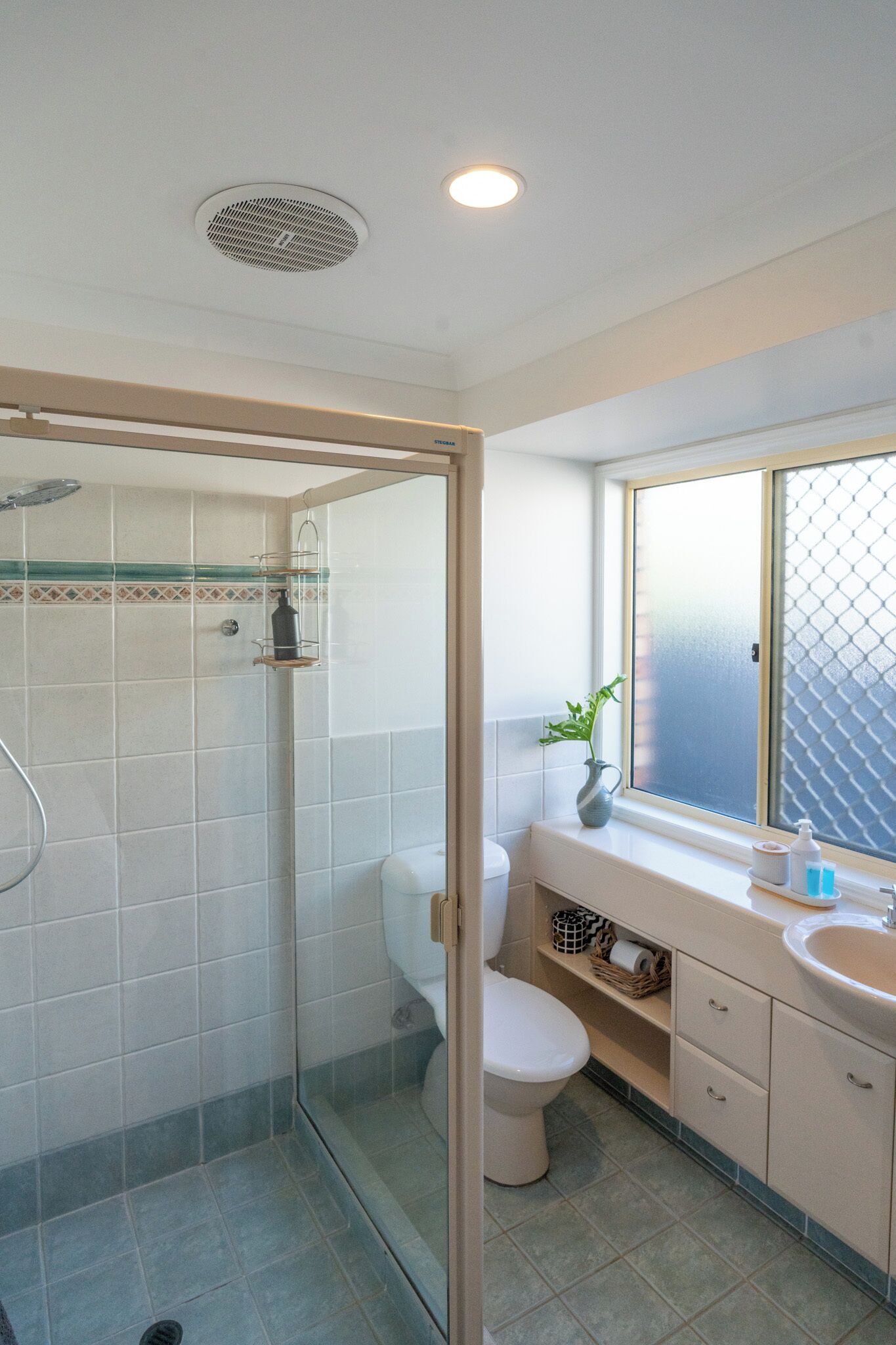 Un baño moderno con ducha de vidrio, inodoro y lavabo con ventana arriba.