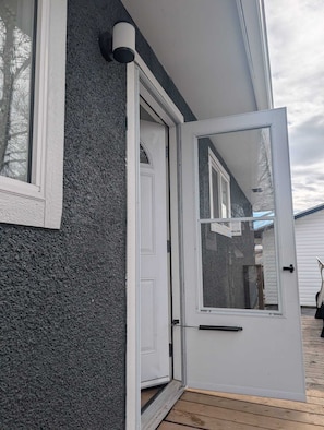 A house with a white door, a window, and a grey exterior wall.