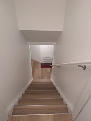 A staircase with wooden steps and white walls, leading to a room with a radiator and a red rug.