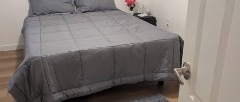 A bedroom with a bed, a nightstand, a wall socket, and a door.