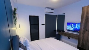 Un dormitorio moderno con cama, televisor, espejo y puerta.
