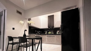 Una cocina moderna con zona de comedor, que presenta un refrigerador negro, armarios blancos y un florero con flores sobre la mesa.