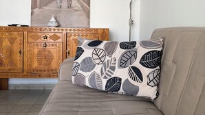 A living room with a beige sofa, a patterned pillow, a wooden cabinet with intricate designs, and a wall-mounted lamp. - 5 minutes to the centre of Algiers center (Alger Centre)