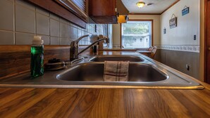 A kitchen with a wooden countertop, stainless steel sink, and a window with blinds. - Waterfront Cabin for up to 8 (Benton)