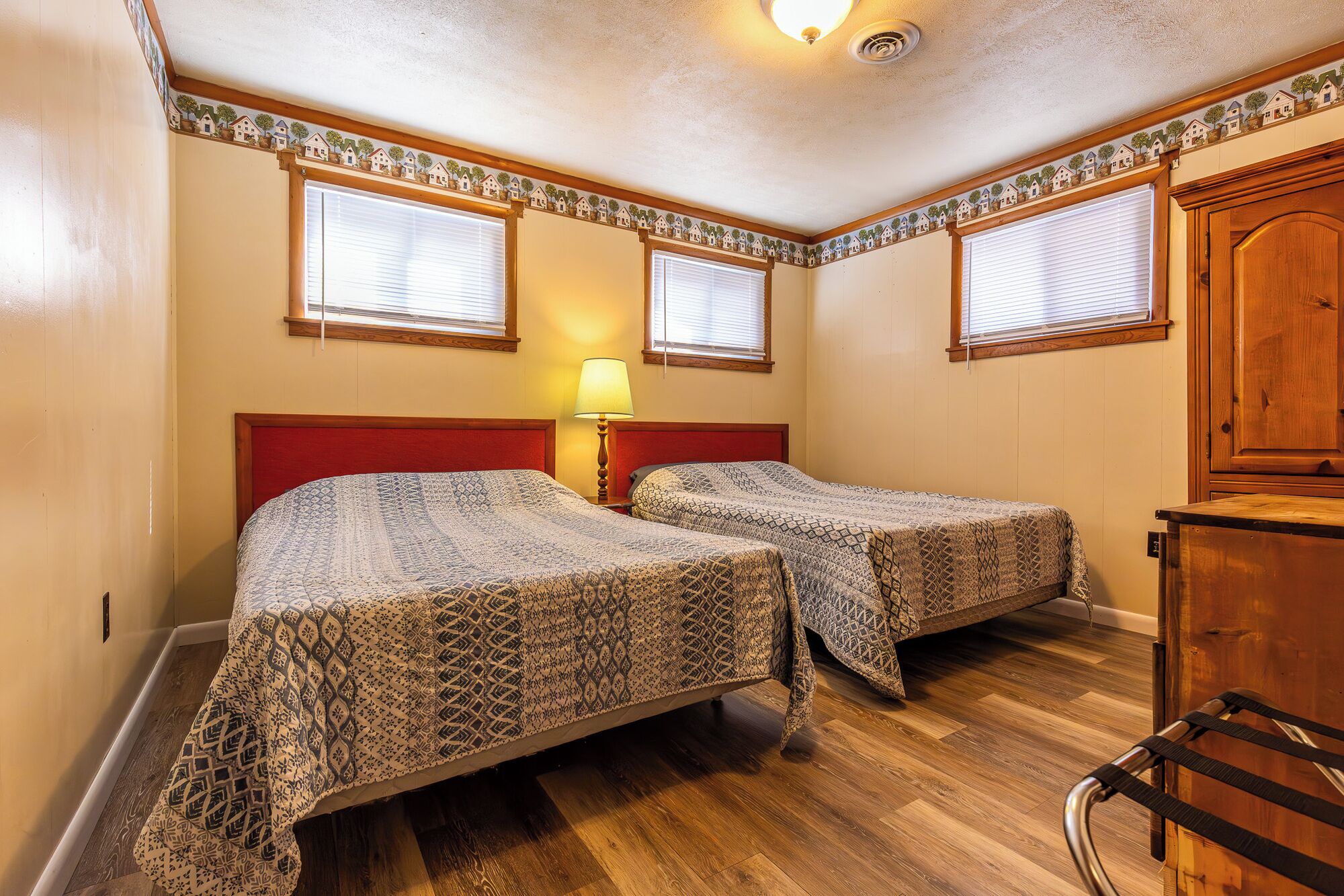 Une chambre avec deux lits, un plancher en bois, une armoire en bois et une lampe.