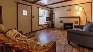 A cozy living room with a fireplace, a television on a wooden stand, and a wicker sofa. - Waterfront Cabin for up to 8 (Benton)
