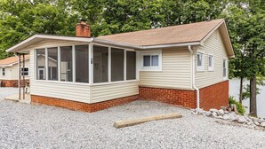 A single-story house with a covered porch, a brick foundation, and a small attached garage. - Waterfront Cabin for up to 8 (Benton)