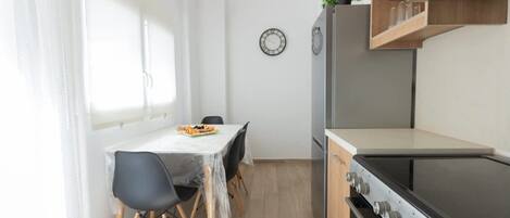 A compact kitchen with a dining table, chairs, a stove, and a clock on the wall.