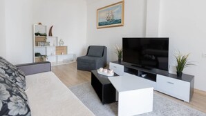 A modern living room with a sofa, a coffee table, a TV, and a bookshelf. - Le Plaza Modern Escape Near Thessaloniki Center (Kalamaria)
