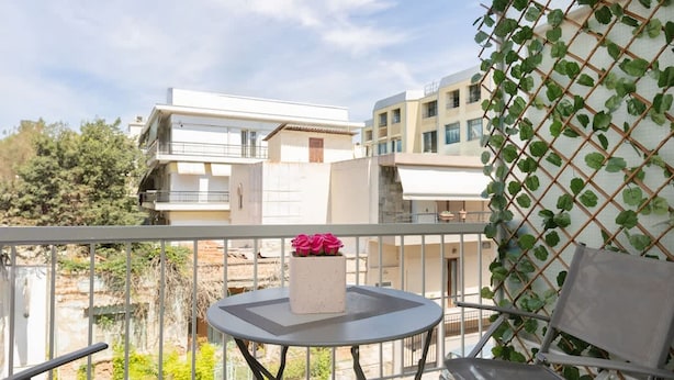 A balcony with a table and chair, a white building in the background, and a green climbing plant on the right. - Le Plaza Modern Escape Near Thessaloniki Center (Kalamaria)
