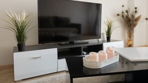 A modern living room with a flat-screen TV, a white cabinet, a black coffee table, and two potted plants. - Le Plaza Modern Escape Near Thessaloniki Center (Kalamaria)