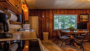 A compact kitchen with wooden cabinets, a refrigerator, a coffee maker, and a dining area with a table and chairs. - Waterfront Cabin for up to 6 (Benton)