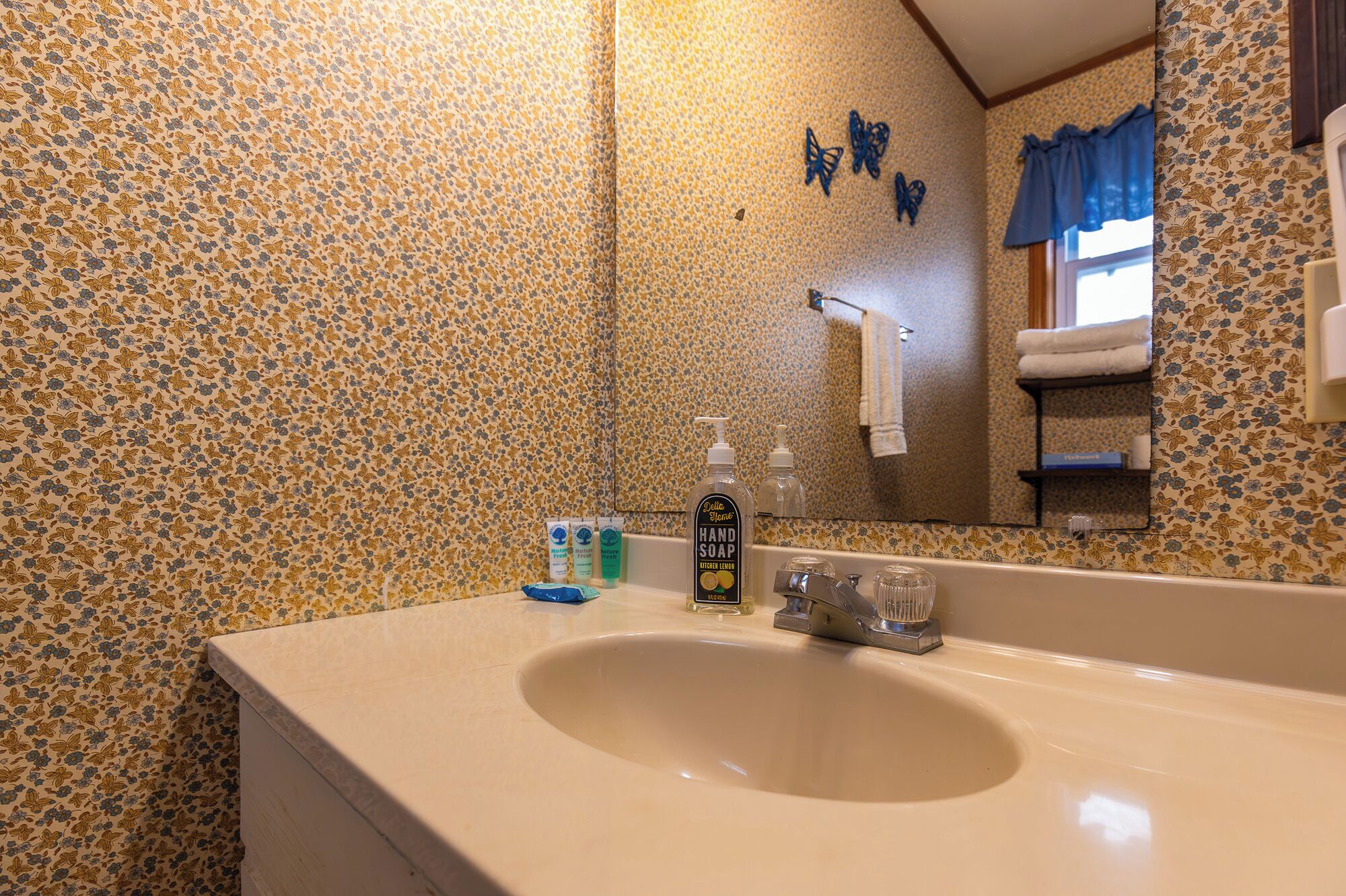 A bathroom with a floral patterned wall, a sink with a mirror, and toiletries on the counter.