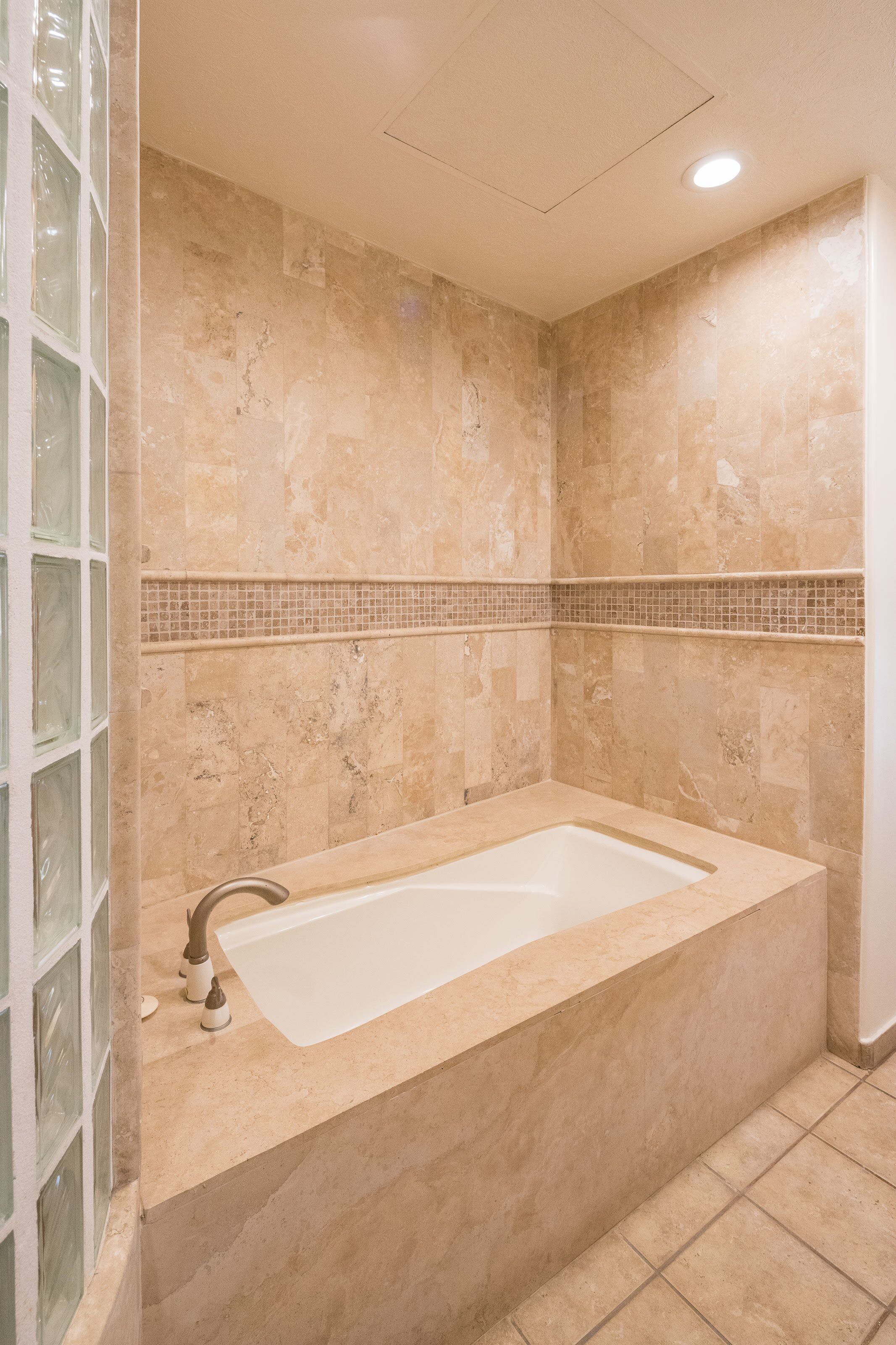 Une salle de bain dotée d’une grande baignoire, de murs carrelés et d’une cabine de douche en verre.