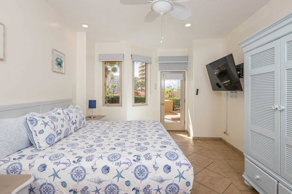 A bedroom with a bed, a ceiling fan, a TV mounted on the wall, and a wardrobe.