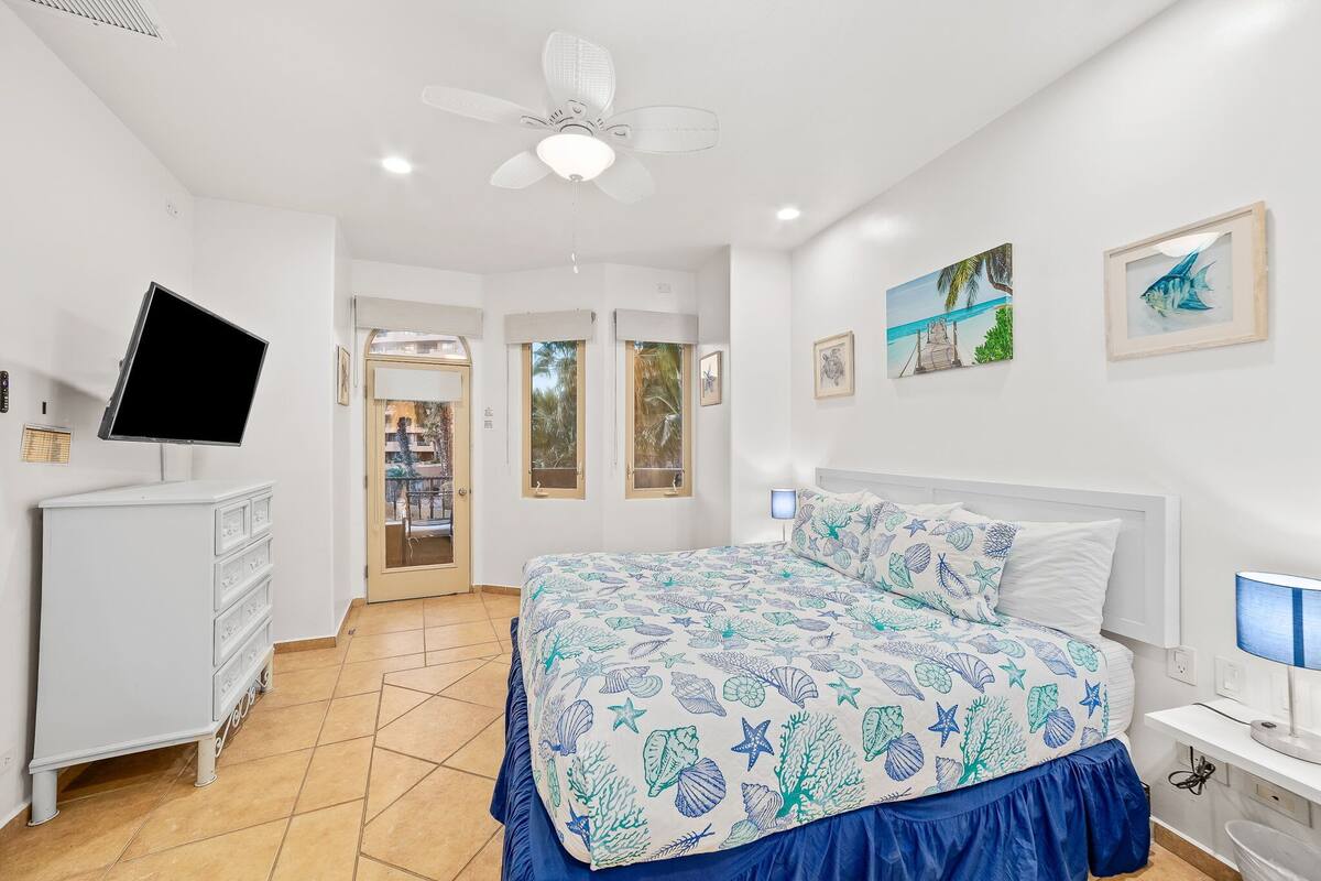 A bedroom with a bed, a dresser, a desk with a lamp, and two framed pictures on the wall.