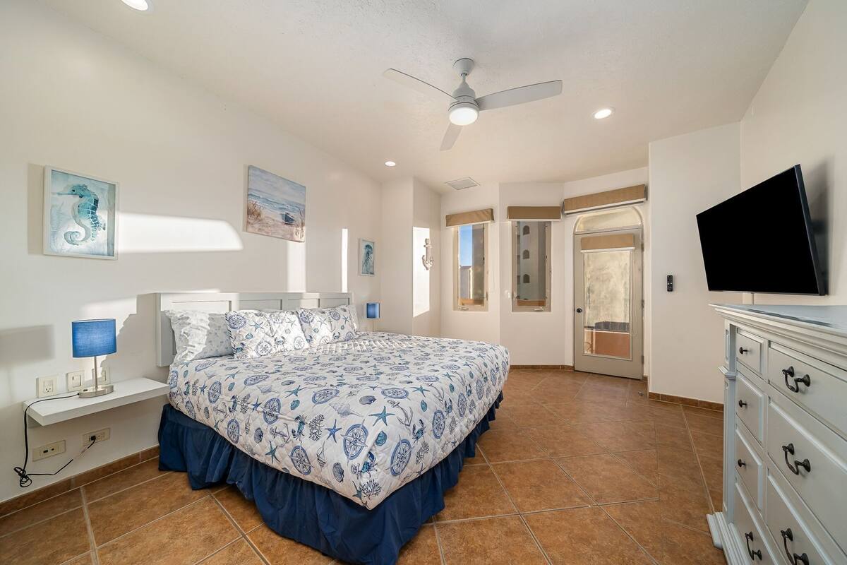 A bedroom with a bed, a ceiling fan, a TV, and artwork on the walls.
