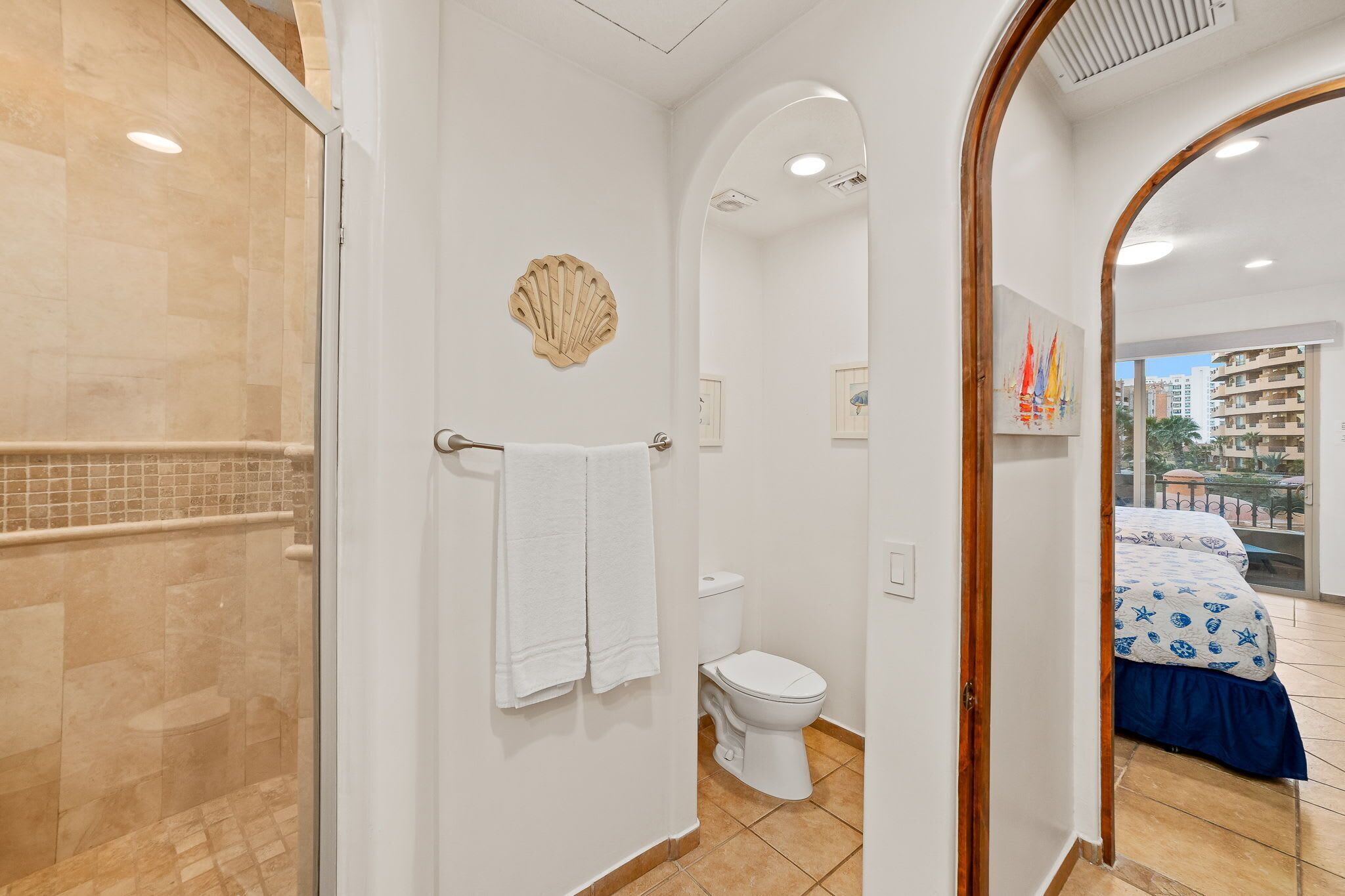 Un baño con cabina de ducha de vidrio, inodoro y cama con colcha de rayas azules y blancas.
