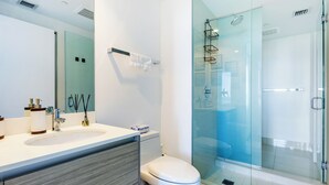 A modern bathroom with a glass-enclosed shower, a white sink, and a toilet. - High Rise Condo Water Views Walker's Paradise (Miami)