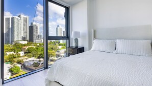 A modern bedroom with a large window, a bed, a nightstand, and a lamp. - High Rise Condo Water Views Walker's Paradise (Miami)