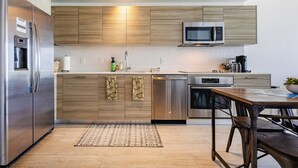 A modern kitchen with wooden cabinets, stainless steel appliances, and a dining area with a table and chairs. - High Rise Condo Water Views Walker's Paradise (Miami)