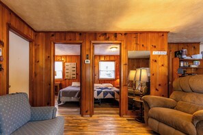 Une cabane aux murs en bois, un lit recouvert d’une courtepointe, un canapé bleu à motifs et un canapé marron.