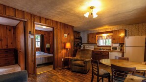 Una camera accogliente in stile baita, con un letto, una sedia, un tavolo da pranzo e un angolo cottura con mobili e elettrodomestici in legno.
