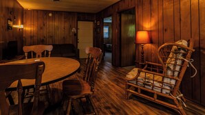 Een houten interieur met een ronde tafel, stoelen, een bank en een rieten stoel.